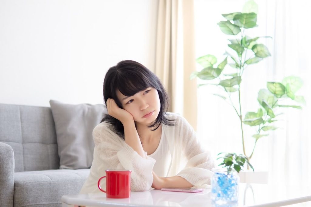 部屋の中で悩み暗い顔をする女性 | 縁結びサロン「ゆるり」